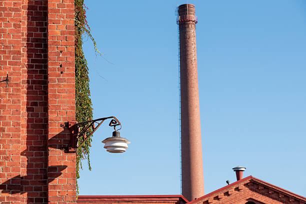 An old red brick factory with a tall industrial chimney under a bright blue sky. The clean lines, repeating brick patterns and classic chimney silhouette make this image suitable for themes of industrial history, architecture, manufacturing heritage, urban landscapes and Scandinavian outdoor scenes.