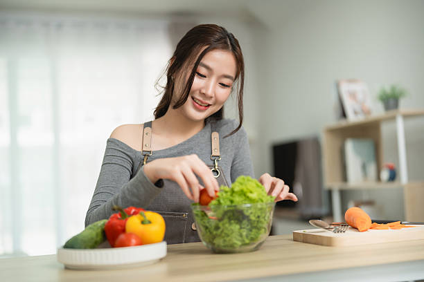 Young woman prepares fresh salad in modern kitchen with vibrant vegetables, enjoying healthy lifestyle and culinary creativity in home environment