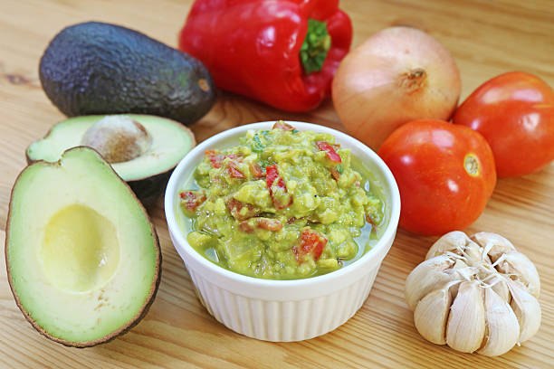 Ingredients for avocado dip flying and falling in stone bowl lemon, coriander, chili, garlic, tomato, sliced nachos in Mexico