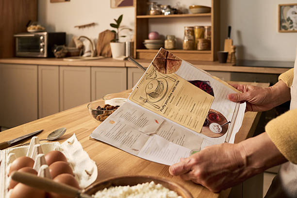 istock Middle Aged Woman Reading Recipe Book While Preparing Ingredients 2240053330