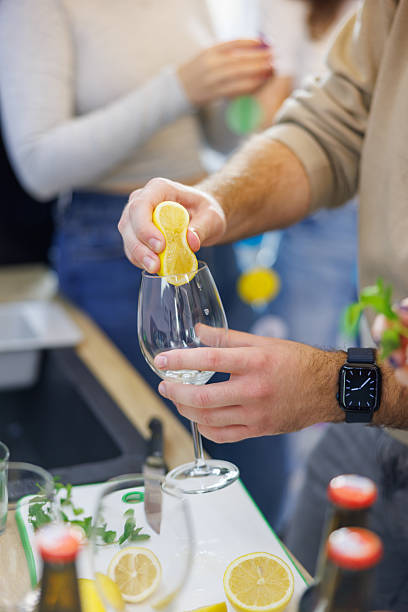 Standing by the kitchen counter and squeezing lemon in glass for non-alcoholic beverage, hanging out in the kitchen before the party