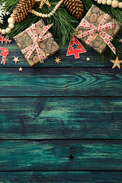 istock Festive flat lay with two wrapped gifts, pine branches, pinecones, red reindeer and tree cutouts on rustic teal wood, cozy Christmas background for design. 2240055232