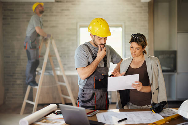 istock Female inspector and manual worker reading plans at renovating home. 2240058145