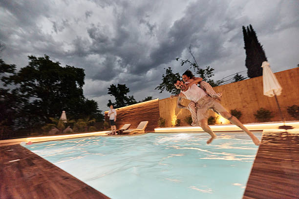 istock Carefree couple having fun while jumping in the pool at night. 2240059780