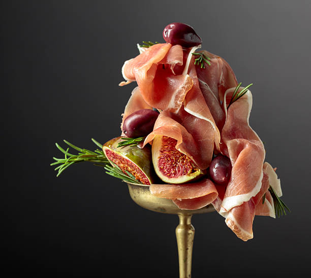 Prosciutto with figs, rosemary, and red olives in an old brass dish.