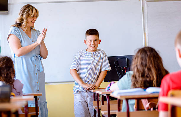 istock Smiling teacher assisting young boy with assignment at school. 2240065915