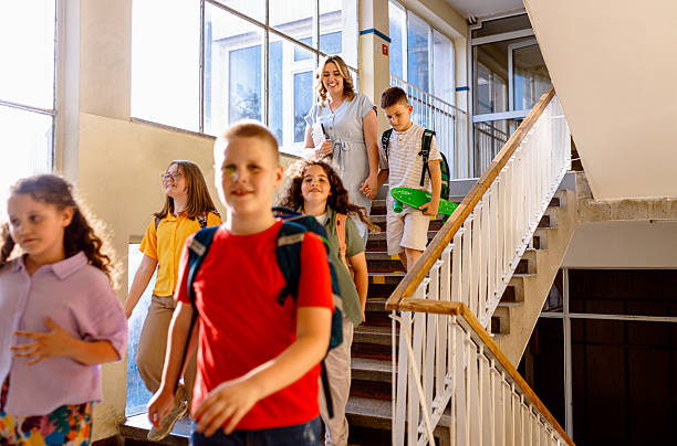 istock Teacher with schoolkids walking on stairs on school hallway. 2240065921