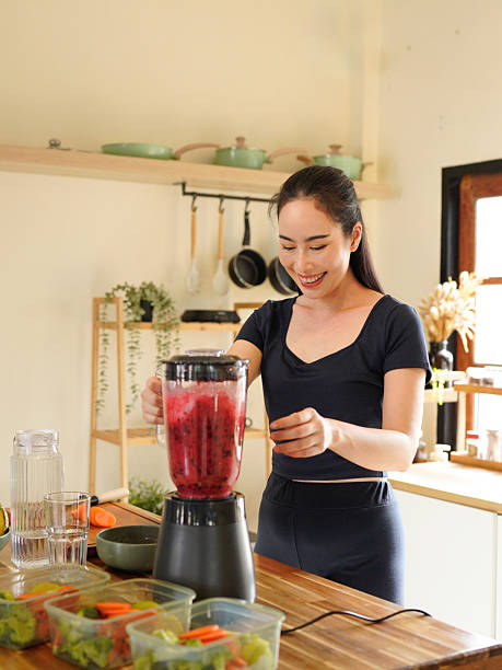 istock Smiling woman making a colorful fruit smoothie in a blender at a bright kitchen setting on the counter, surrounded by fruit and vegetable 2240068275