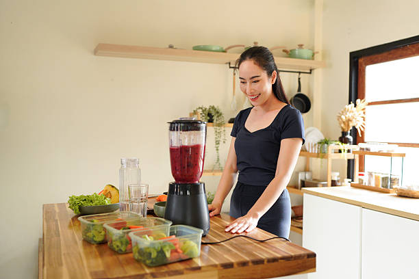 istock Smiling woman making a colorful fruit smoothie in a blender at a bright kitchen setting on the counter, surrounded by fruit and vegetable 2240068284
