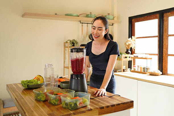 istock Smiling woman making a colorful fruit smoothie in a blender at a bright kitchen setting on the counter, surrounded by fruit and vegetable 2240068290