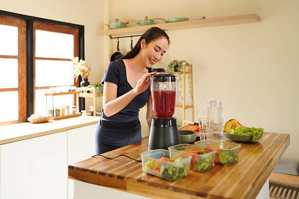 istock A happy young woman smiles brightly while preparing a healthy red smoothie in her kitchen, surrounded by fresh fruits and vegetables. 2240068297