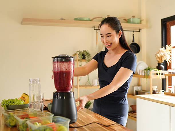 istock Smiling woman making a colorful fruit smoothie in a blender at a bright kitchen setting on the counter, surrounded by fruit and vegetable 2240068306