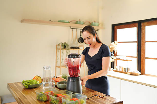 istock Smiling woman making a colorful fruit smoothie in a blender at a bright kitchen setting on the counter, surrounded by fruit and vegetable 2240068541