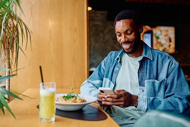 istock Smiling Black man using phone during lunch in restaurant 2240068981