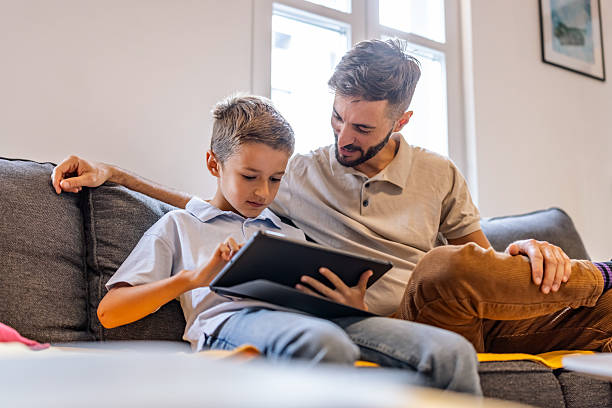 istock Father And Son Reading Tablet Together On Couch For Family Learning Moment 2240069987