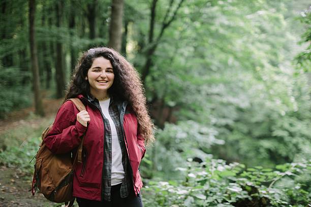 istock Young woman smiling carrying backpack hiking in forest 2240070110