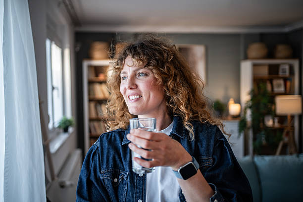 istock Woman smiling drinking water looking out window at home 2240070703