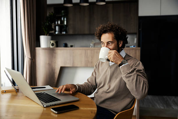 istock Man drinking coffee working on laptop at home 2240071865