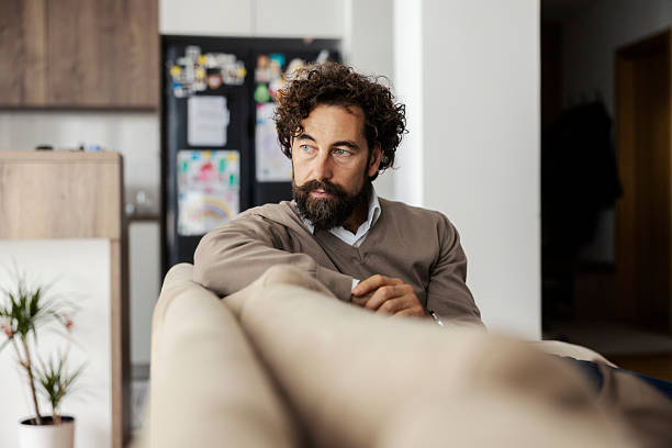 Thoughtful man sitting on couch at home contemplating