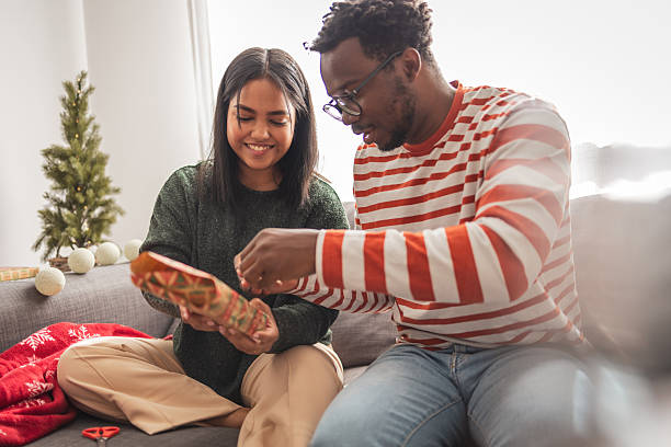 istock Young couple wrapping christmas gift together on sofa 2240073150