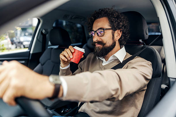 istock Middle aged man driving car drinking coffee 2240073410