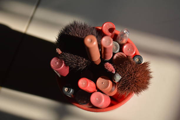 A collection of makeup brushes and cosmetic tools organized in a red holder on a sunlit vanity table. Soft light enhances colors and textures, highlighting beauty essentials for personal care and makeup artistry.