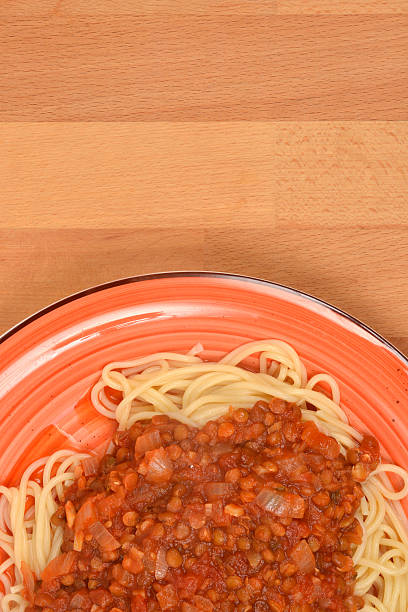 An overhead shot of a plate of spaghetti topped with thick, rich vegan lentil Bolognese sauce, served on an orange dish on a wooden background