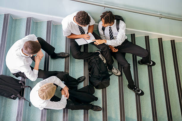 istock Four high school boys sitting on steps in school building, one with notebook 2240076749