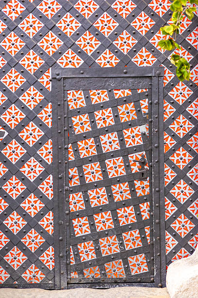 istock A decorative door with a patterned design in shades of black and red. Surrounding plants add a touch of greenery to the entrance. 2240077323