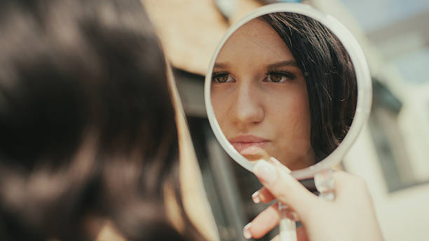 istock Young woman applies makeup with handheld mirror during daytime 2240080682