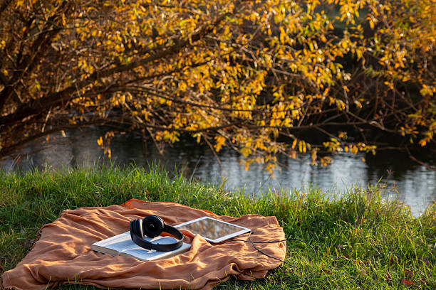 istock Autumn relaxation with book, headphones, tablet by river 2240083160