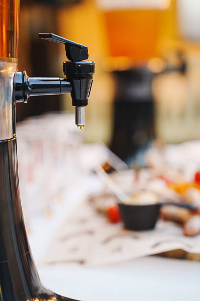 A beverage dispenser stands ready to serve drinks at a lively outdoor event. Colorful food is spread across the table, creating a cheerful atmosphere during the gathering.