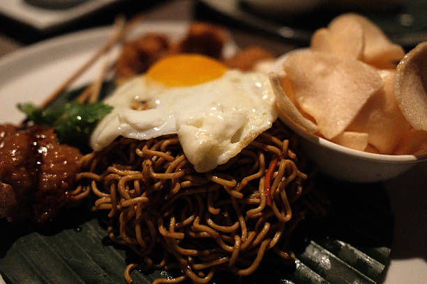 Indonesian Mie Goreng, fried noodles served with a sunny-side-up egg, chicken satay, and prawn crackers