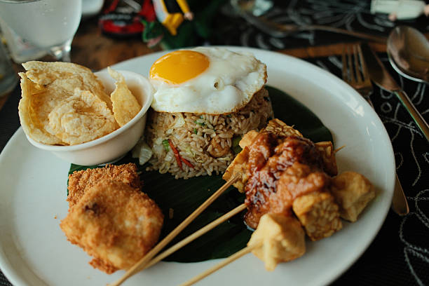 Nasi Goreng, a traditional Indonesian fried rice dish, served with a fried egg, satay skewers, and crispy crackers