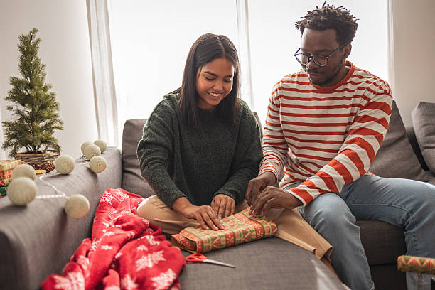 istock Young couple wrapping christmas presents on sofa 2240084304