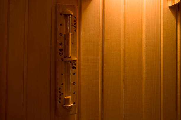 A person pours water over hot sauna rocks, creating steam in a traditional wooden sauna. The image highlights the soothing and rejuvenating experience of sauna bathing, with visible wooden floors and relaxing ambiance.