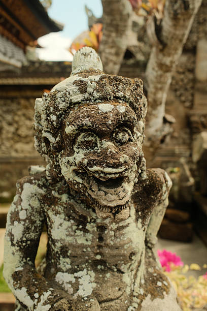 Weathered religious sculpture of a Balinese guardian protecting a Hindu temple, covered in moss and lichen