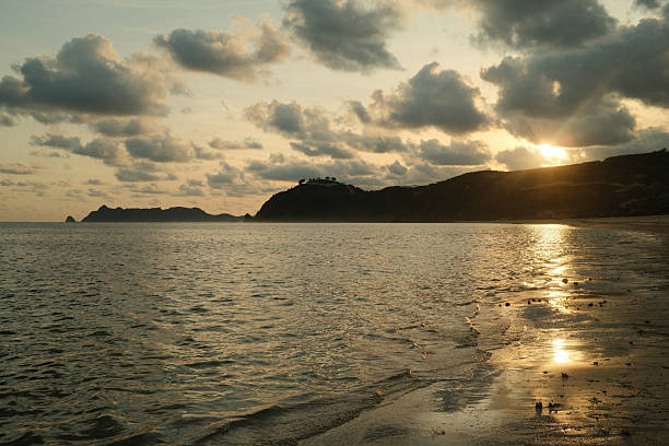Golden sunbeams breaking through clouds and reflecting on a calm ocean at sunset, showing a serene coastal landscape