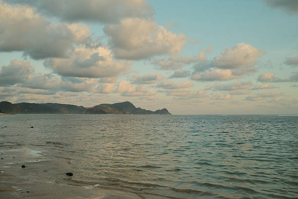 Quiet beach scene featuring gentle ocean waves, distant mountains, and soft clouds at dusk, offering a relaxing nature view