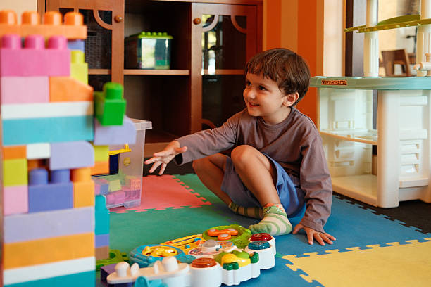 Young boy smiling, sitting on a playmat, and reaching for colorful building blocks and toys in a playroom