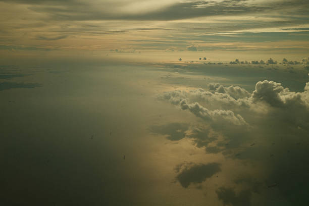 Aerial view discovering ocean surface, scattered cumulus clouds, and small ships during a hazy golden hour sunset
