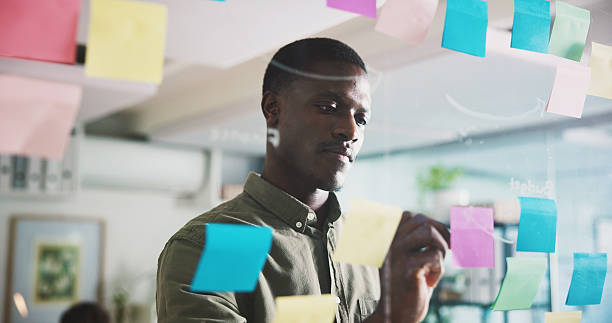 istock Writing, brainstorming and person in office with sticky note, ideas or solution for project management. Planning, mindmap or black man in workplace with problem solving, business insight or strategy 2240085922