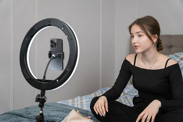 istock Young girl creating engaging video content in her cozy bedroom, using a smartphone and ring light to record a tutorial, embodying the modern influencer lifestyle 2240087886