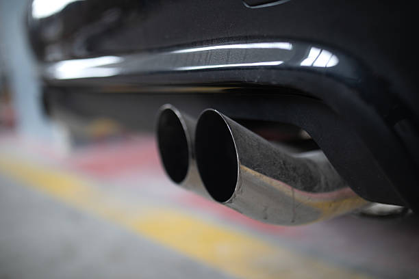 Car exhaust pipe emits dense smoke during emission test on city pavement. Pollution control device measures harmful gases. Service car center garage workshop.  Automobile repair check up diagnosis.