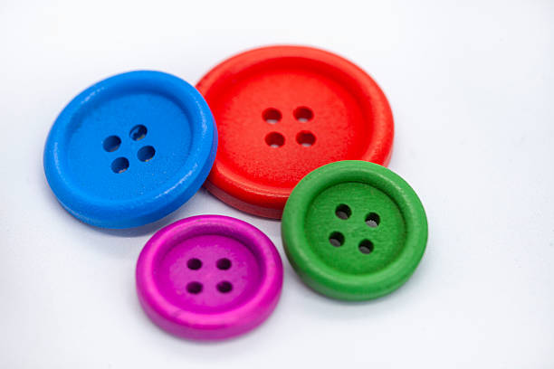 Four buttons of different colors are arranged on a white surface with selective focus. The buttons are green, red, blue, and purple