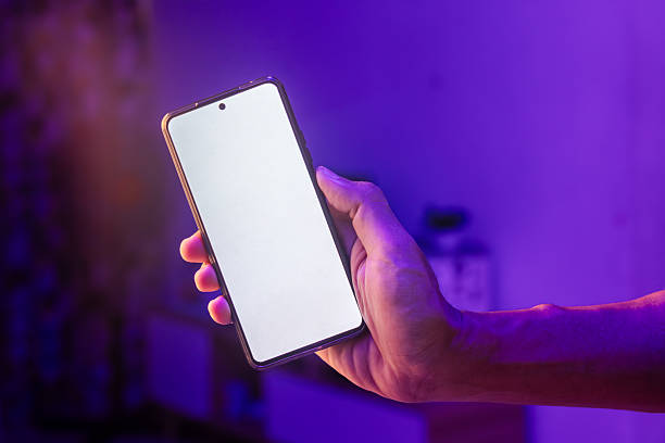 istock Man's hand showing smartphone with blank screen on blue and purple neon lights background 2240102254