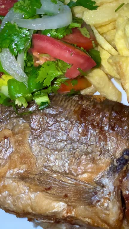 A close-up shot of fried potatoes, fried fish, and a salad with fresh vegetables and herbs. Cooking delicious food at home.