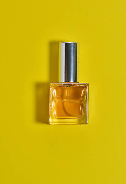 istock Square perfume bottle with a silver metal cap. The bottle is centered on a bright yellow background 2240104661