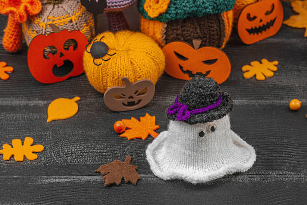 Cozy Halloween scene with cute ghost figurines in tiny hats. Handmade knitted autumn decor, crocheted pumpkins, fall leaves, berries, spiders, and ghosts. Dark brick background, place for text