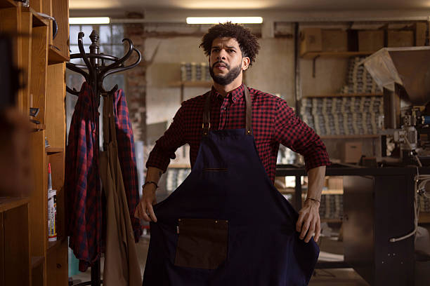 istock Craftsman in Workshop Wearing Navy Apron Over Red Plaid Shirt Surrounded by Tools 2240106006